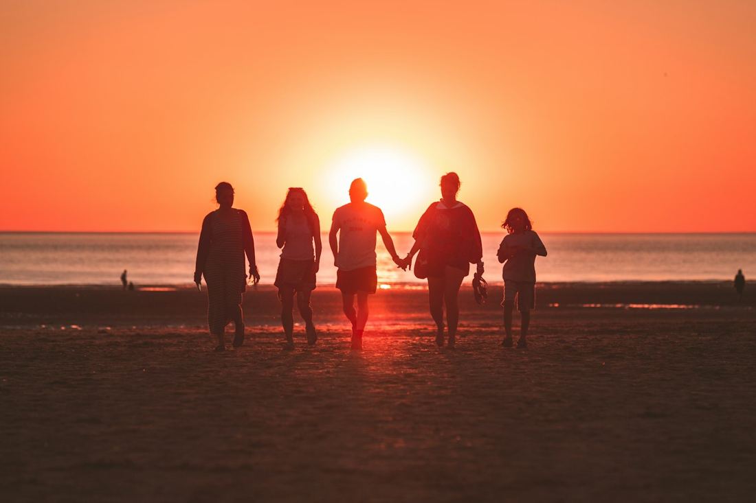 Família caminhando na praia ao pôr do sol